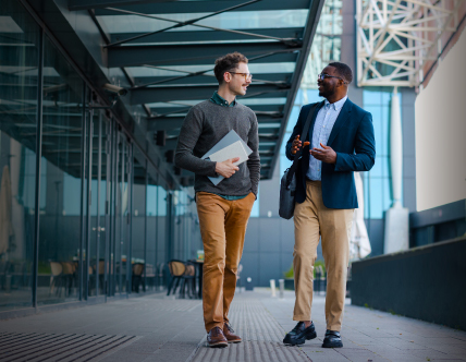 Two gentlemen walking and discussing outside a building 
