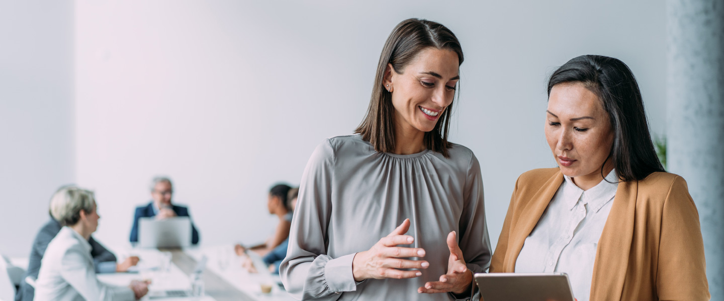 two women looking at tablet in conference room