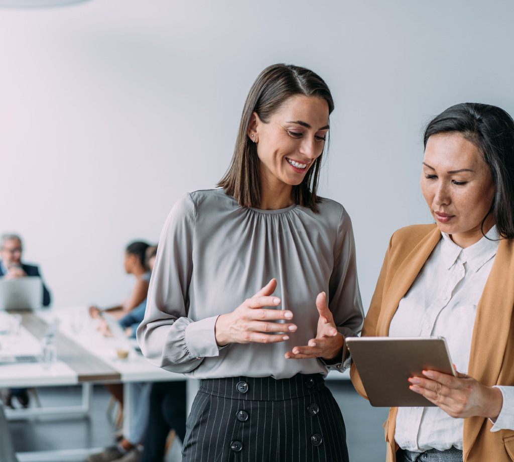 two women looking at tablet in conference room